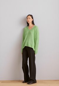Bright green, oversized, wool sweater with a V-neck and long sleeves, paired with black wide-leg trousers and dark footwear.