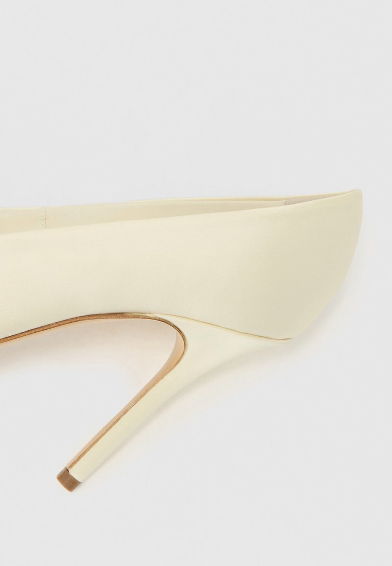 Beiger Satin-Pumps mit spitzer Kappe und schlankem Stiletto-Absatz. Glatte Textur mit einem kontrastierenden, metallischen Akzent an der Absatzspitze.