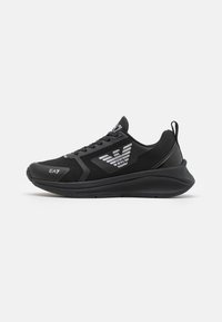 Zapatillas deportivas negras con parte superior de malla, suela de goma y cuello acolchado. Presentan un logo en contraste y un diseño elegante con acentos texturizados.