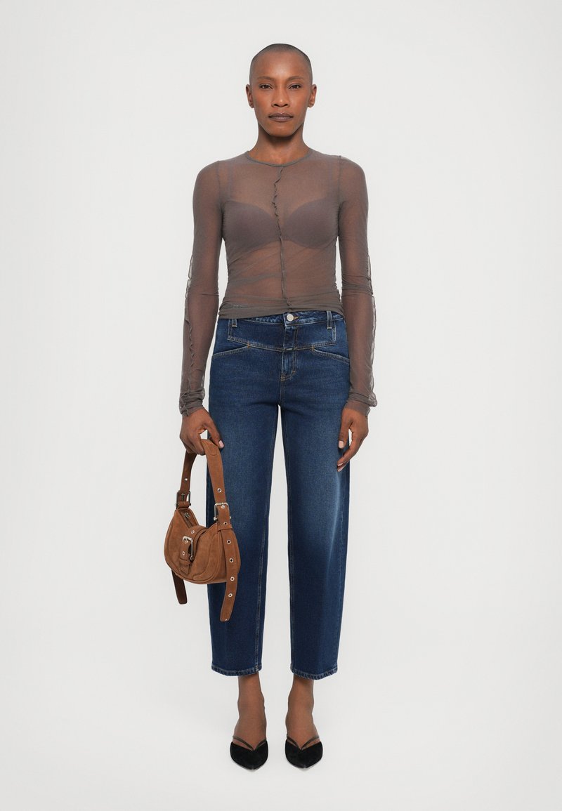 Sheer gray long-sleeve top with button detail, high-waisted blue denim jeans, and a brown suede handbag, featuring a rounded shape and strap.