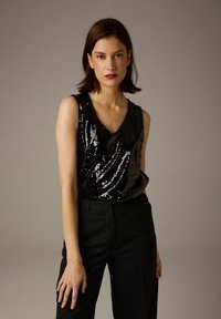 Haut noir sans manches recouvert de sequins réfléchissants avec un décolleté en V, assorti à un pantalon noir ajusté à fines rayures discrètes.