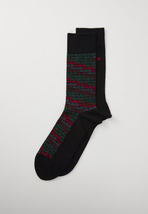 Une paire de chaussettes noires avec un motif textuel répétitif "HUGO" multicolore en rouge, vert et gris sur le devant.