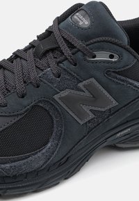 Black athletic shoe with a combination of smooth leather and textured mesh. Features a prominent 'N' logo and thick outsole for cushioning.