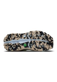 Suela texturizada de un zapato en beige y negro, con tacos multidireccionales para ofrecer tracción, con un logo visible y un detalle en acento verde.