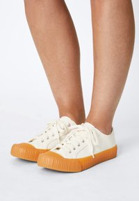 Canvas sneakers in off-white with a textured rubber orange sole; features metal eyelets and laces; rounded toe design.