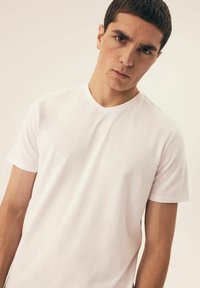 Biała koszulka z krótkim rękawem i dekoltem w serek, wykonana z gładkiego bawełnianego materiału, charakteryzująca się luźnym krojem i schludnymi detalami w szwie.