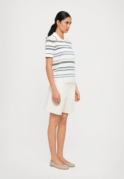 Polo bianco con righe multicolori, abbinato a pantaloni corti crema. Tessuto morbido, maniche corte e vestibilità rilassata.