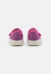 Sapatos de tecido cor-de-rosa com um upper texturizado, tiras elásticas e solas de borracha branca, apresentando um acabamento suave e uma forma arredondada.