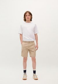 Maglietta bianca a maniche corte abbinata a pantaloni cargo beige con tasche laterali. Indossata con calzini fantasiosi e sneakers color tortora.