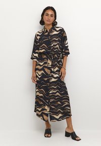 Vestido abotonado en azul oscuro con patrones ondulados en beige y marrón, ceñido a la cintura con un lazo. Mangas cortas y longitud midi.