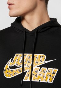 Black hoodie featuring a large, colorful leopard-print Nike logo with white accents. The material appears soft with a classic design and adjustable hood.