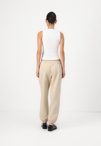 Top branco canelado sem mangas emparelhado com calças de moletom largas bege, apresentando um cós elástico e punhos franzidos, complementado por sapatos pretos.