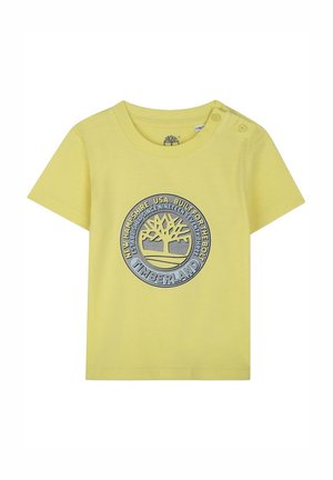 Yellow cotton T-shirt with short sleeves, featuring a circular, blue and gray Timberland logo and two snap buttons on the left shoulder.