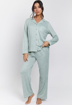 Green patterned pajama set with long sleeves and loose pants. Features a buttoned shirt with a pocket, accented by white trim. Soft fabric texture.