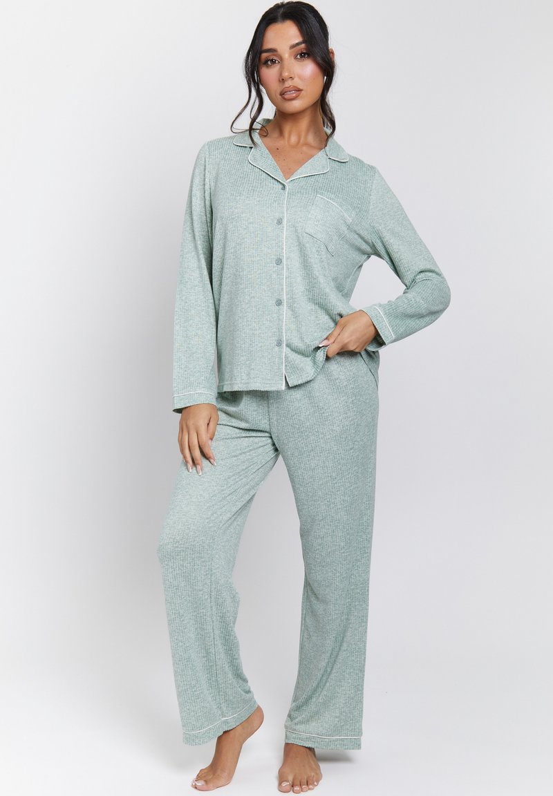Conjunto de pijama verde con estampado, de mangas largas y pantalones holgados. Incluye una camisa abotonada con un bolsillo, acentuada con ribetes blancos. Textura de tela suave.