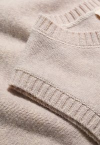 Világos bézs pulóver, puha gyapjóból készült. Bordás nyakkivágással és mandzsettákkal rendelkezik, sima textúrájú, enyhén bolyhos felülettel.