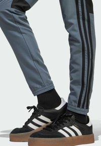 Svartvita lädersneakers med gummisula, tillsammans med grå träningsbyxor med svarta ränder och elastiska muddar.