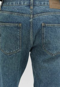 Jeans i denim med en medelblå tvätt, fem fickor och sömsdetaljer. Tyget har en strukturerad yta med en hållbar känsla.