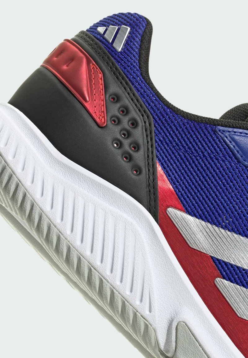 Buty sportowe z teksturowanym niebieskim wierzchem, czarnym obcasem, czerwonymi akcentami i białą podeszwą z rowkami dla lepszej przyczepności. Ozdobione srebrnym logo.