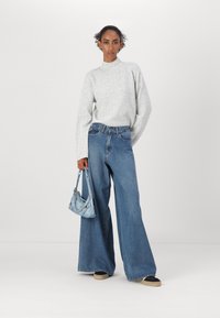 Vide bukser i denim i mellemblå farve, parret med en lysegrå kabelstrikket sweater og en lille lyseblå håndtaske. Sneakers fuldender outfittet.