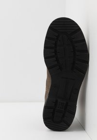 Bota de cuero marrón con una suela de goma negra. Presenta un patrón de tracción texturizado y costuras visibles a lo largo de la parte superior.