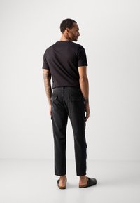 Maglietta nera, pantaloni cargo in denim scuro, tasche visibili, scarpe casual slip-on, design minimale, sfondo neutro.