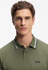 Zielona koszulka polo z teksturowanej tkaniny, z plisą na trzy guziki, kołnierzykiem w kontrastowe czarno-białe paski oraz haftowanym logo "BOSS".
