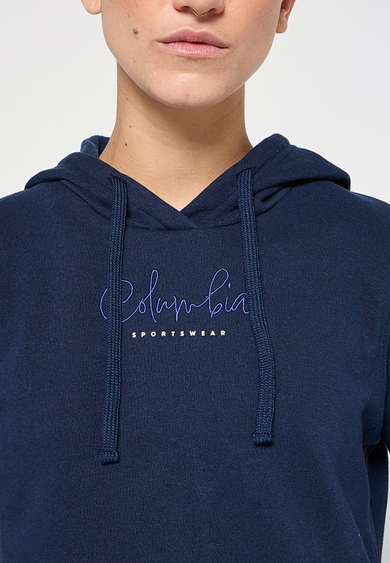 Felpa con cappuccio di colore blu navy con lacci, presenta il logo "Columbia Sportswear" ricamato in bianco e viola sulla parte anteriore. Tessuto morbido, vestibilità standard.