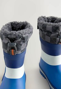 Blaue Gummistiefel mit einem weißen Streifen, ausgestattet mit einem grauen, gesteppelten Bündchen und grauem Futter. Enthält eine graue Kordel zum Verstellen.