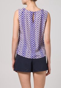 Top bez rękawów w niebiesko-kremowy zygzakowaty wzór, z wycięciem w kształcie klucza z tyłu. Wykonany z lekkiego materiału, zestawiony z ciemnymi szortami.