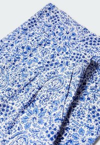 Valkoinen kangas, jossa on monimutkaisia sinisiä kukka- ja paisley-kuvioita, sileä tekstuuri ja taitettu muotoilu, joka esittelee kankaan rosoa.