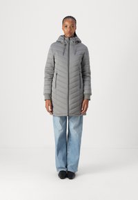 Grå pufferjakke med hette, som har et chevron-sy mønster, frontglidelås og sidelommer. Kombinert med lyseblå, vide jeans.