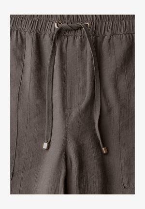 Pantaloni marroni, texture, con vita elasticizzata, dotati di un cordoncino con accessori metallici dorati e tasche laterali discrete.