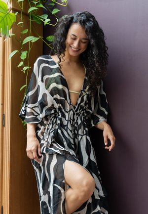 Vloeiende zwart-witte kimono met abstracte golfpatronen; doorschijnende stof, diepe V-hals, strakke taille en een zijsplit, die een lichtgroene detail eronder onthult.