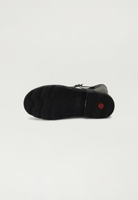 Suela de zapatilla de goma negra con patrón texturizado en zigzag, acento rojo y detalle de logo. Presenta un diseño de agarre duradero y flexible.