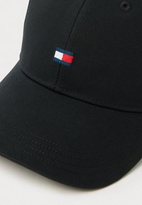 Fekete baseball sapka ívelt napellenzővel, az elején egy kis hímzett zászlólogóval piros, fehér és kék színekben. Simas textúrájú anyag.
