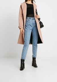 Lång rosa kappa över en svart texturerad topp, kombinerad med högmidjade blå jeans och svarta stövlar med klack. Inkluderar en liten svart handväska.