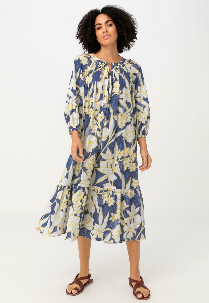 Kleid mit floralem Muster, langärmlig in Marineblau und Creme, mit gelben Akzenten. Verfügt über einen Schlüssel-Ausschnitt und einen gestuften Saum, aus leichtem Stoff gefertigt.