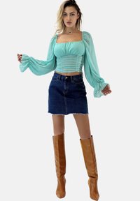 Top verde menta a maniche lunghe con scollatura quadrata e dettagli arricciati, abbinato a una minigonna in denim scuro e stivali marroni al ginocchio.
