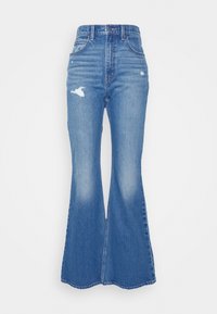 Jean évasé taille haute en denim bleu clair, avec des détails usés et un effet délavé. Design classique à cinq poches, fermeture éclair à l'avant.