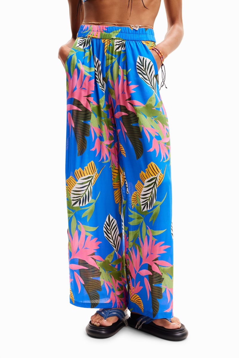 Blauwe wijde broek met een tropisch bladerenpatroon in roze, groen en zwart. Heeft een elastische tailleband en zijzakken.