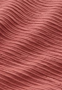 Měkká, vlnitá texturovaná tkanina v barvě prachově růžové s horizontálními hřebeny vytvářející zvlněný, hmatový povrch.