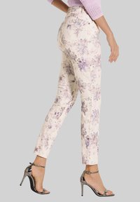Blumenmusterhosen in hellem Creme mit lila und lavendelfarbenen Akzenten. Verfügt über eine taillierte Passform und Gesäßtaschen, kombiniert mit silbernen Absätzen.