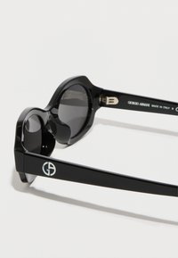 Gafas de sol negras con montura gruesa y redondeada. Las lentes son oscuras. Presentan un destacado logotipo de Giorgio Armani en el lateral y acentos metálicos.