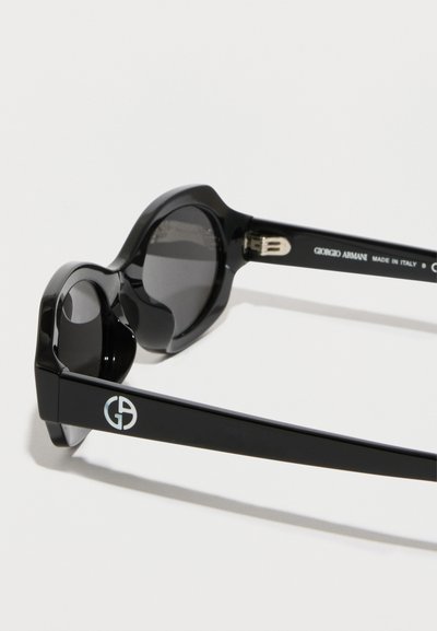 Mustat aurinkolasit paksuilla, pyöristetyillä kehyksillä. Linssit ovat tummat. Sivulla on näkyvä Giorgio Armani -brändäys ja metalliset yksityiskohdat.