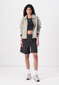 Lichtgrijze ritsjack over een zwarte crop top, gecombineerd met zwarte denim shorts. Het model draagt lichte sneakers en witte sokken.