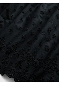 Svart tyg med broderade blommönster i ögla och scallopade kanter, som visar textur och detaljer i närbild.