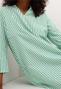 Lekka sukienka w zielono-białe paski z dekoltem w serek i rękawami do połowy łokcia, prezentująca miękką teksturę i luźny krój.