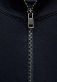 Námornícky zipsový kabát s strieborným kovovým zipsom a obdĺžnikovou ťahacou tablou, ribbovanou textúrou a vysokým dizajnom goliera.