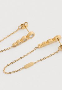 Δαχτυλίδια χρυσής αλυσίδας με τέσσερις στρογγυλούς κρυστάλλους σε βαθμιαία μεγέθη και μια μικρή ορθογώνια ετικέτα χαραγμένη με "LIU·JO" σε λευκό φόντο.